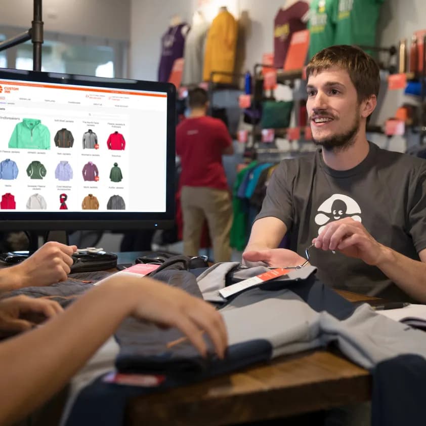 Custom Ink worker wearing an Inky logo t-shirt helps a customer.