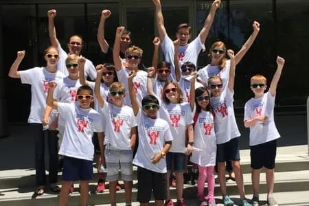 Group of kids and teachers wearing matching custom white computer club t-shirts cheering on steps.