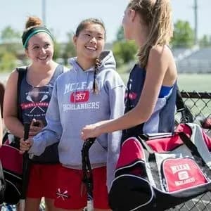 Group girls lacrosse players with custom sports pinnies, shorts, hoodies, and duffel bags.