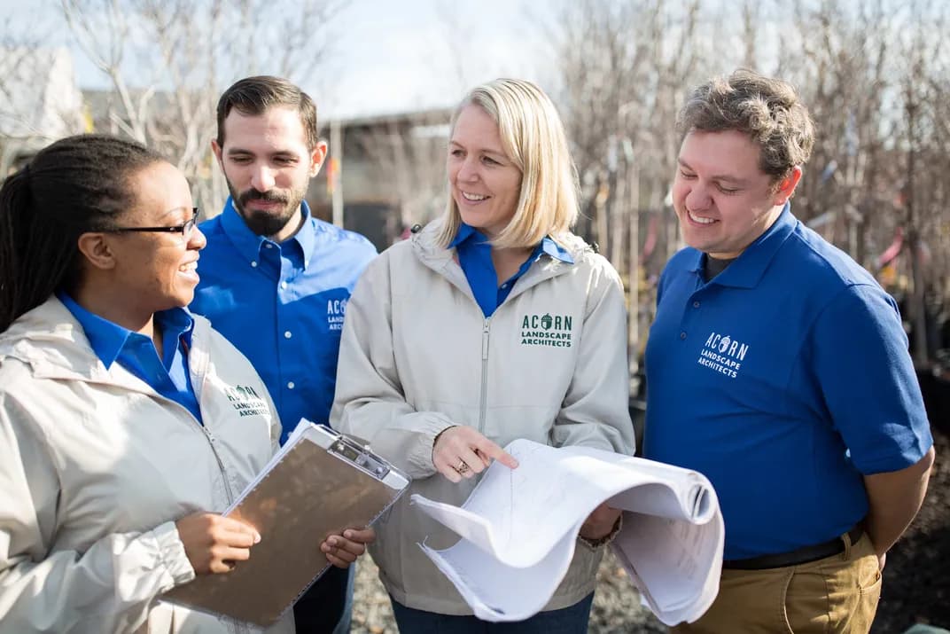 A crew of employees wear coordinated branded apparel for their business 'Acorn Landscape Architects' outdoors.