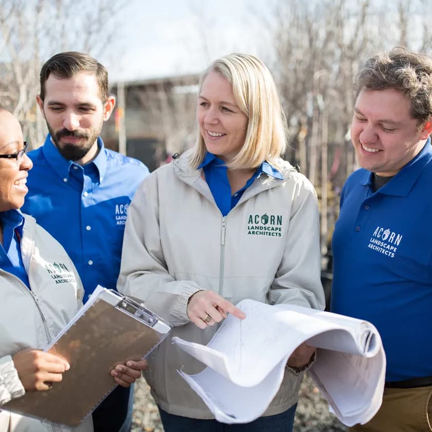 A crew of employees wear coordinated branded apparel for their business 'Acorn Landscape Architects' outdoors.