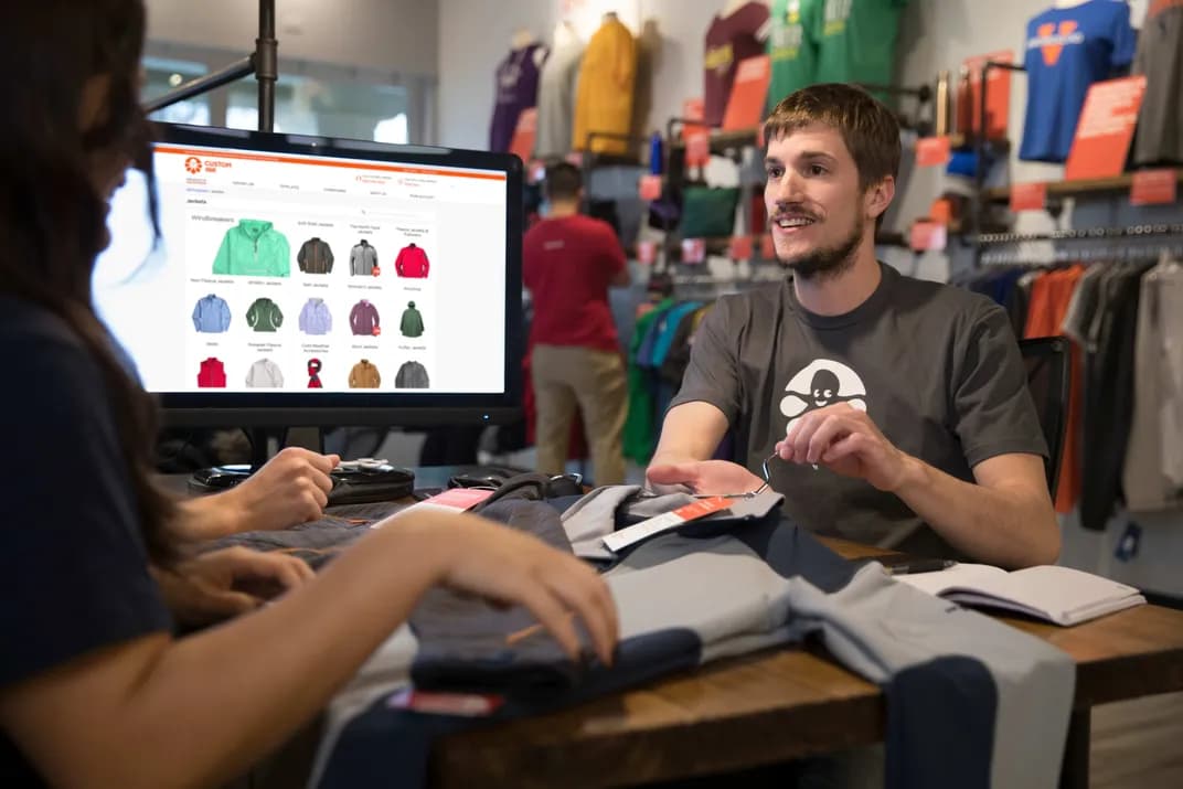 Custom Ink worker wearing an Inky logo t-shirt helps a customer.