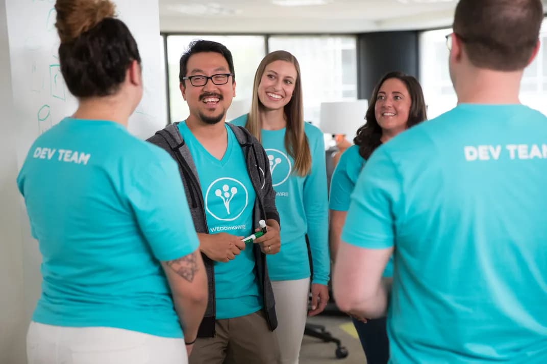 Development team wearing matching custom teal WeddingWire t-shirts collaborating during a meeting.