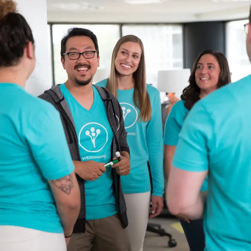 Development team wearing matching custom teal WeddingWire t-shirts collaborating during a meeting.