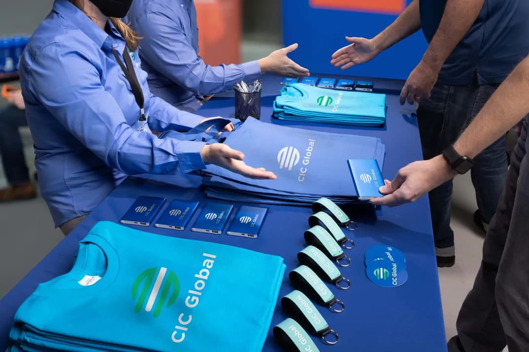 A tradeshow table with custom giveaways, including t-shirts, tote bags, power banks, keychains, pens, and stickers.
