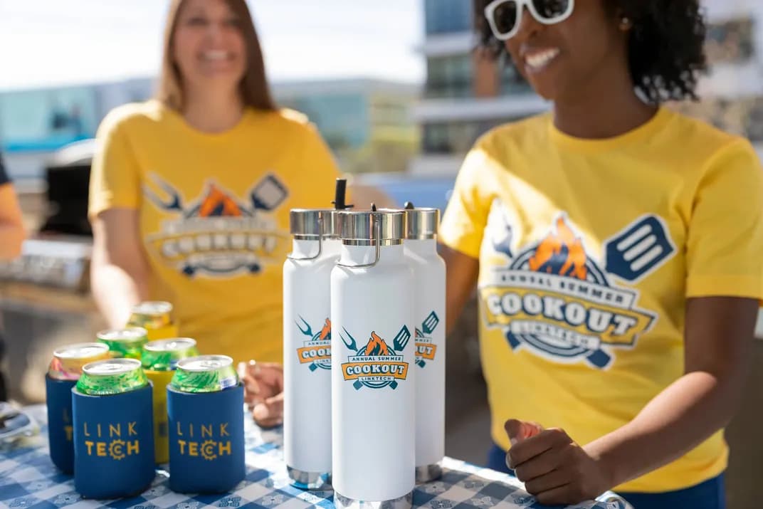 Employees wearing matching custom yellow cookout t-shirts with branded Link Tech drinkware and koozies at a summer event.