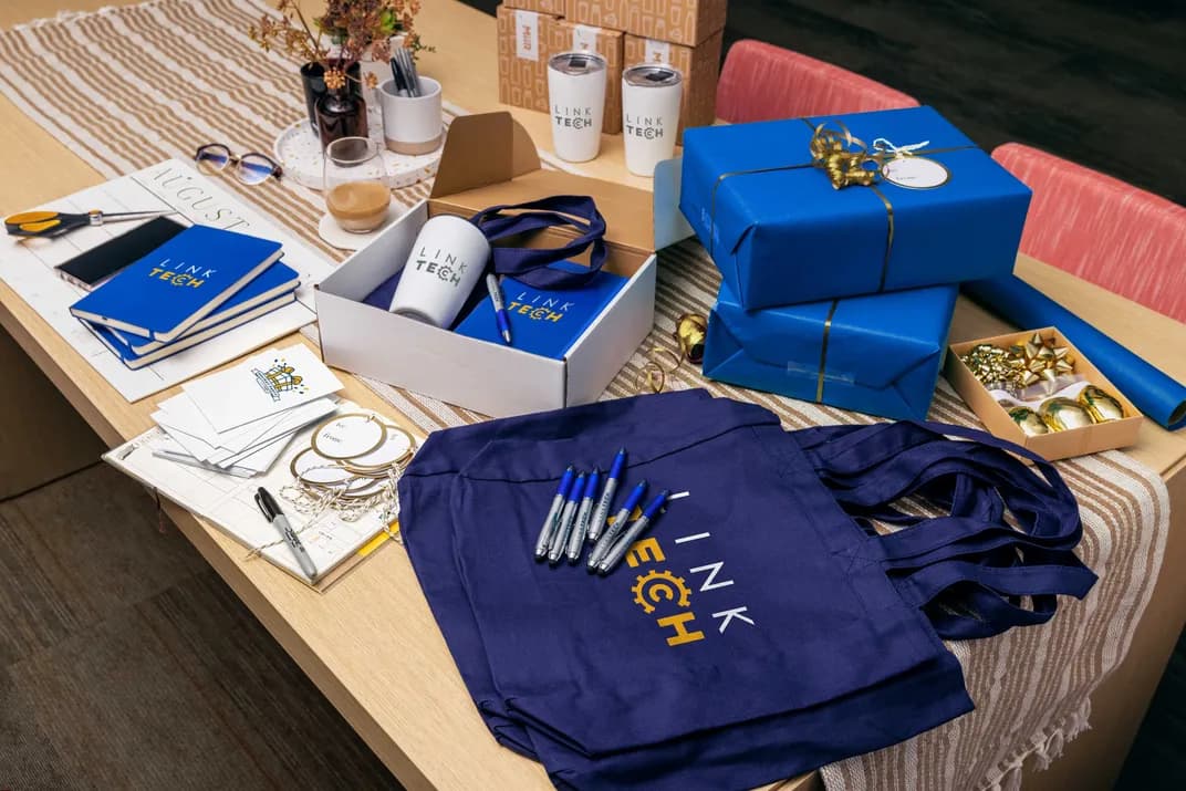 Desk with custom branded Link Tech notebooks, mugs, pens, tote bags, and wrapped gift boxes prepared for corporate gifting.