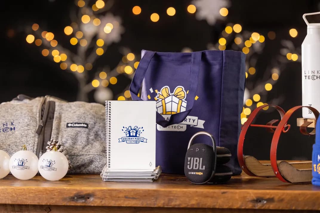 Holiday-themed corporate gifts including custom branded tote bag, jacket, notebook, ornaments, and speaker with Link Tech logo.