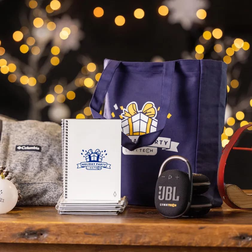 Holiday-themed corporate gifts including custom branded tote bag, jacket, notebook, ornaments, and speaker with Link Tech logo.