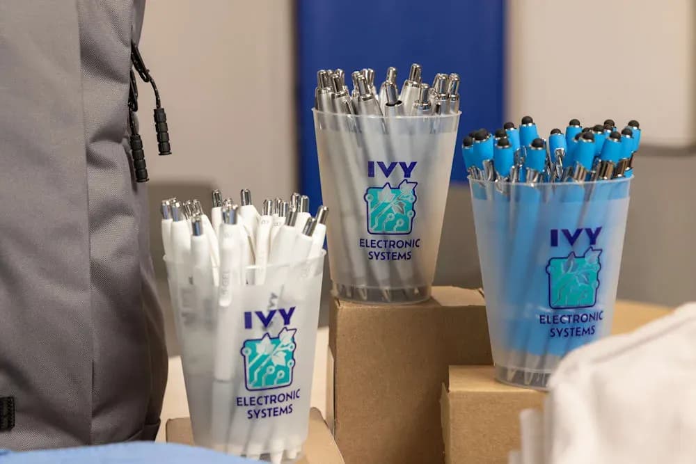 Three branded frosted plastic cups filled with promotional pens on a table display.