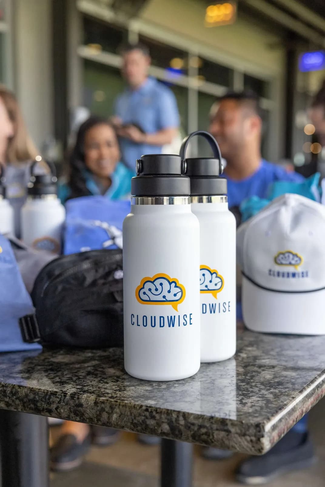Custom branded water bottles and hats with the Cloudwise logo displayed on a table at a company event.