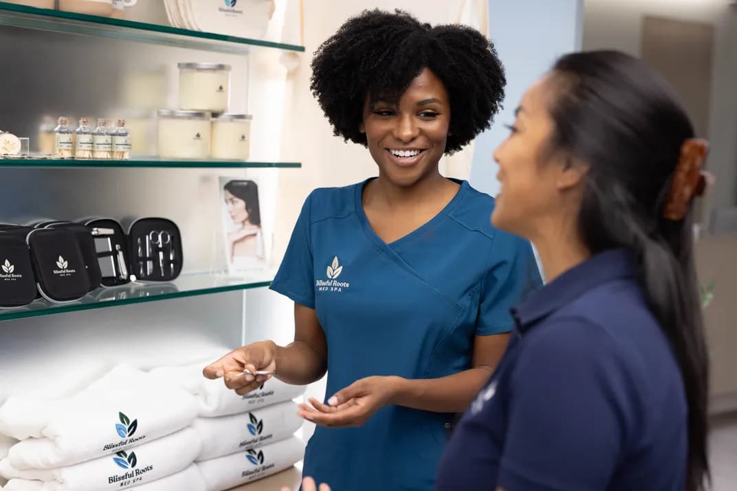 Spa staff wearing branded uniforms with custom logos talk near shelves of promotional merchandise and resale products.