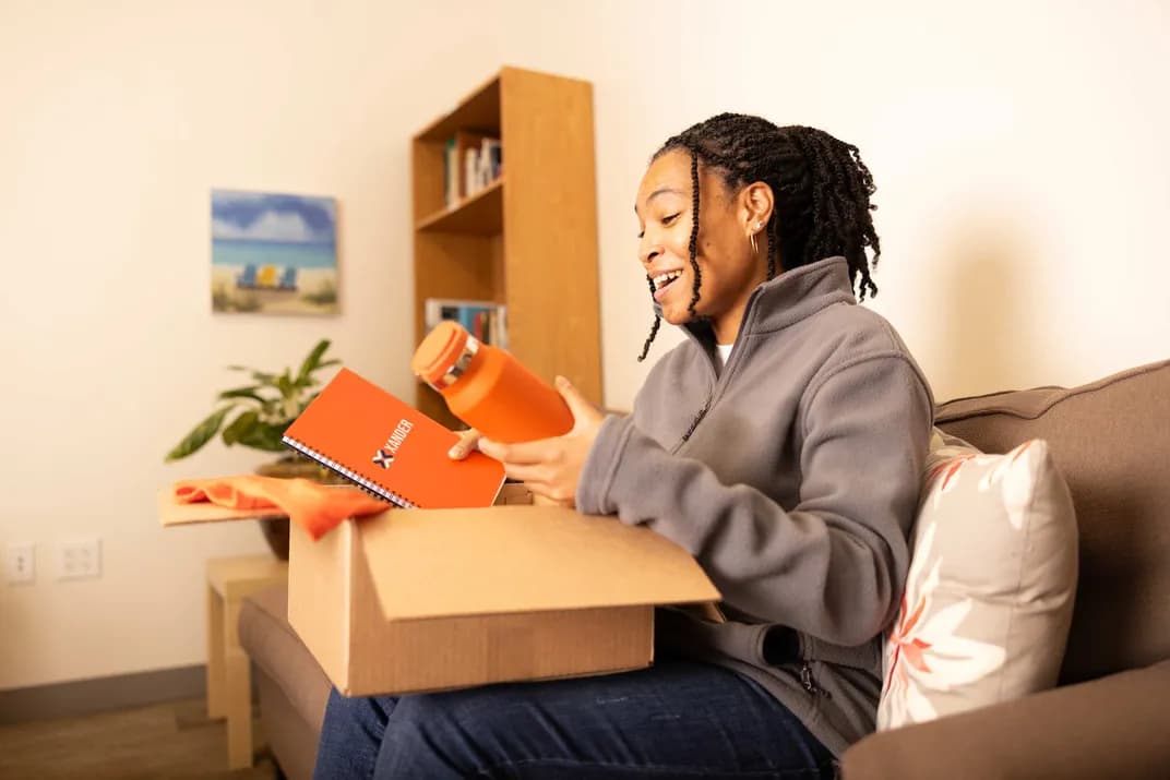 Woman opens a box of branded merchandise, including notebook and water bottle.