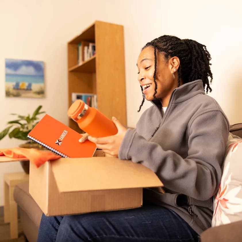 Woman opens a box of branded merchandise, including notebook and water bottle.
