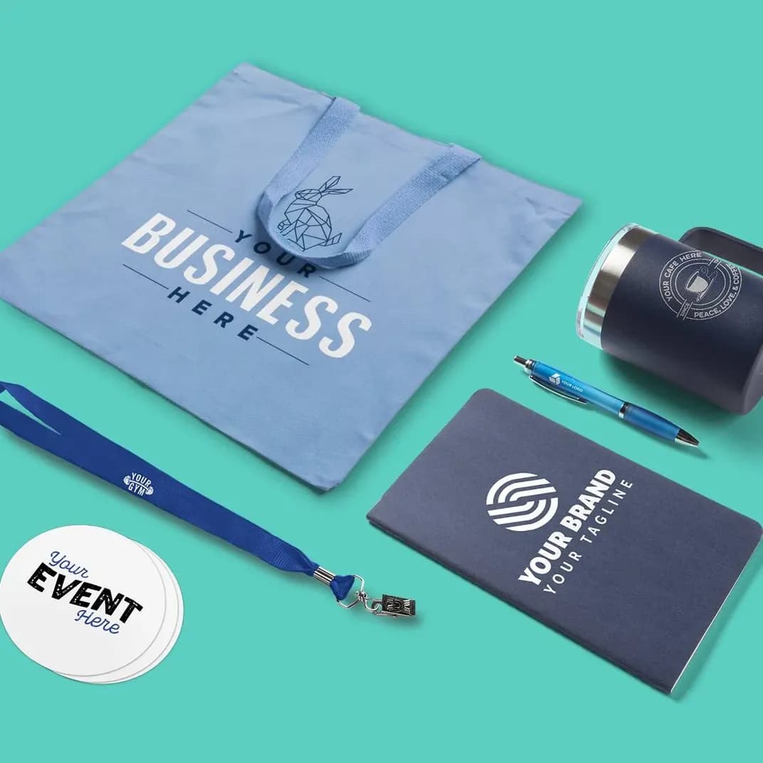 A laydown of branded promotional products including a tote bag, lanyard, notebook, pen, stickers, and insulated mug.