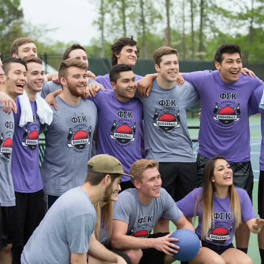 A group of greek fraternity members wearing custom dodgeball designed t-shirts stand on a court.