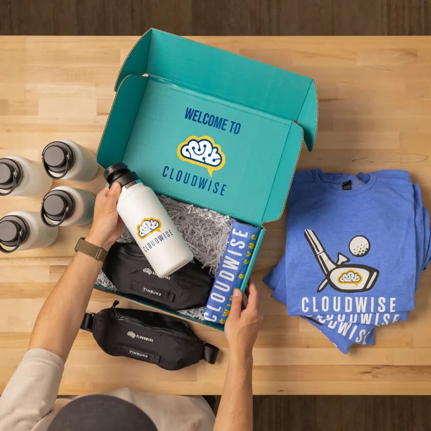 Custom branded mugs and pens featuring the Cloudwise 25 years anniversary logo displayed on a wooden tray