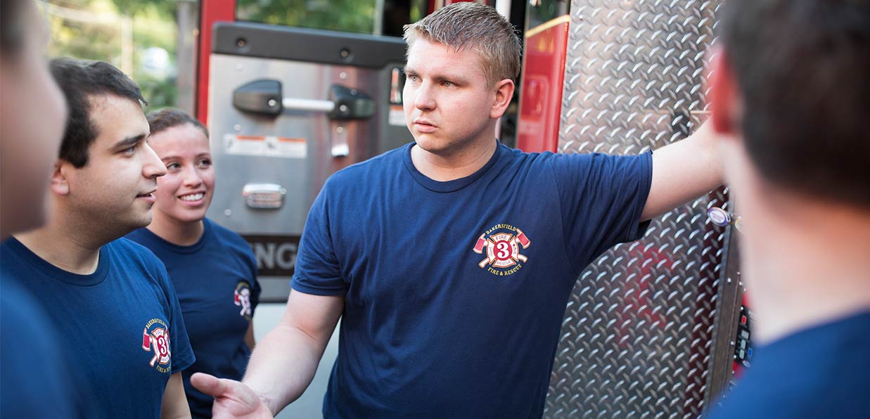 A firefighter and his crew are in custom t-shirts next to a fire truck.