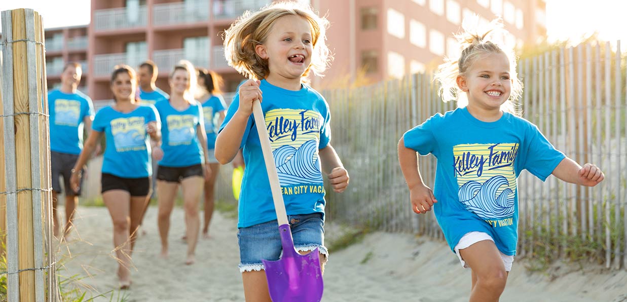A family is walking out the beach together in family vacation t-shirts with two little girls smiling and leading the way.