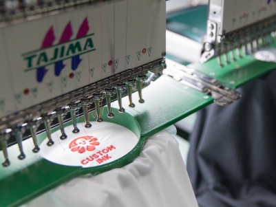An embroidery machine embroiders the Custom Ink logo