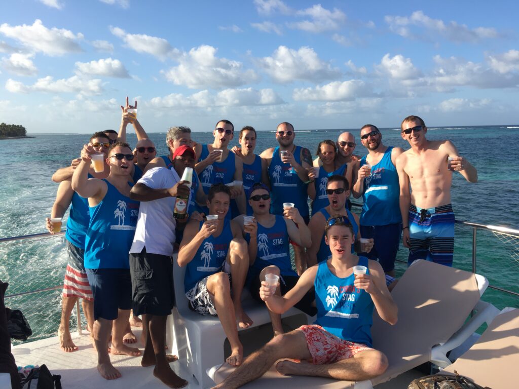 A group of friends celebrating a bachelor party on a boat and wearing their matching custom t-shirts and tank tops. 