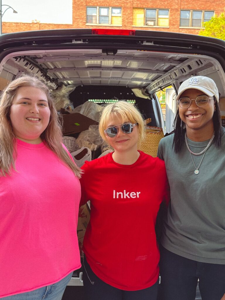 Skylar wears a red "Inker" shirt and stands between two smiling people