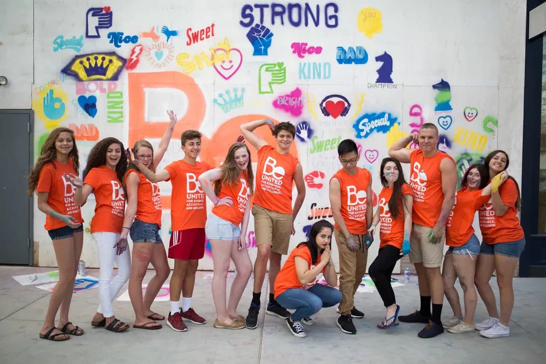 Group of students wearing matching custom orange t-shirts posing in front of a colorful mural.