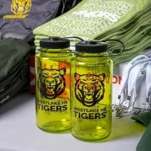 A table of school swag features folded custom t-shirts, decorated water bottles, and lanyards.