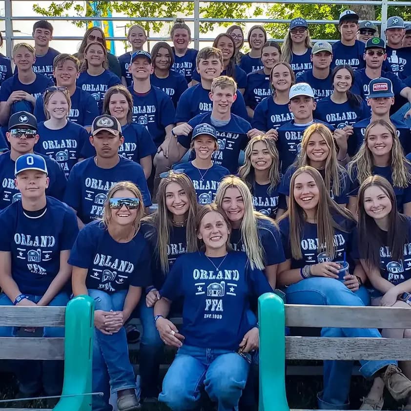Large group of students wearing matching custom navy blue FFA t-shirts posing in bleachers.
