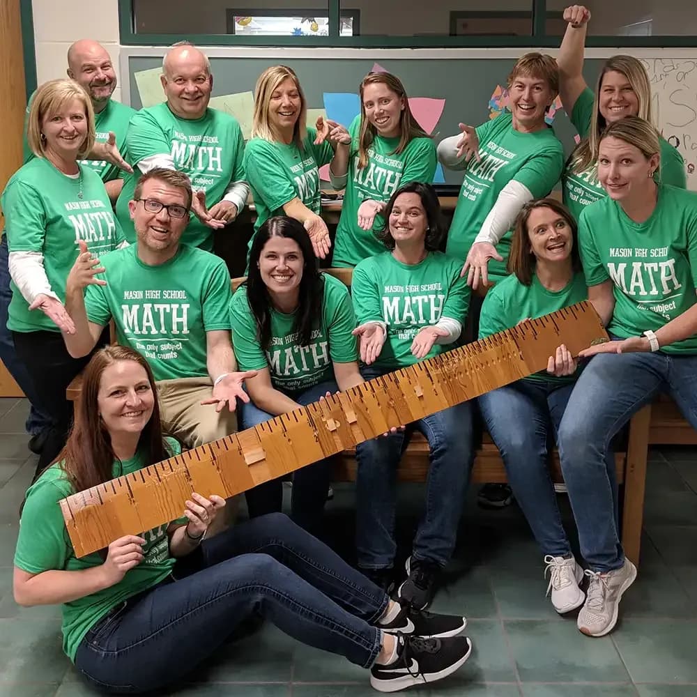 Math teachers wearing matching custom green t-shirts posing with a large wooden ruler.