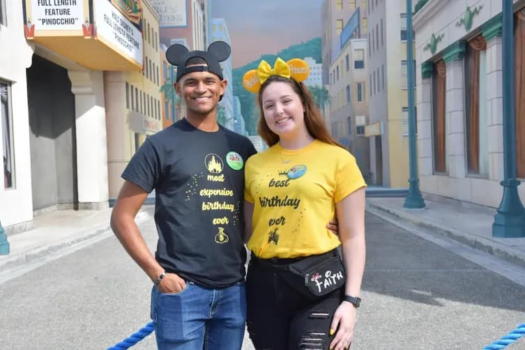 Couple wearing matching custom birthday t-shirts with themed designs at an amusement park.